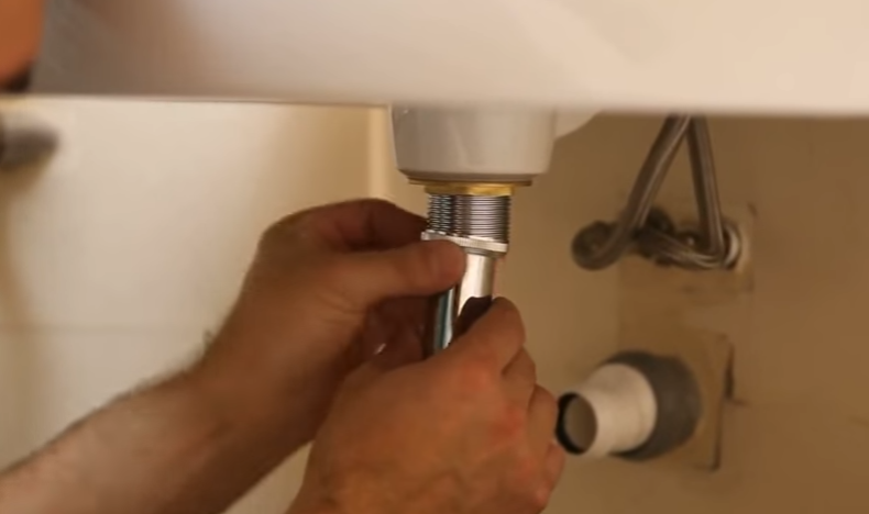 Достаньте из комплекта патрубок, который ведет к самому бутылочному сифону, закрутите верхнюю гайку