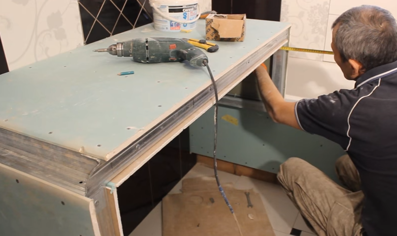 Левая стенка обшита гипсокартоном с обеих сторон, на правой стенке мастер выполняет замеры